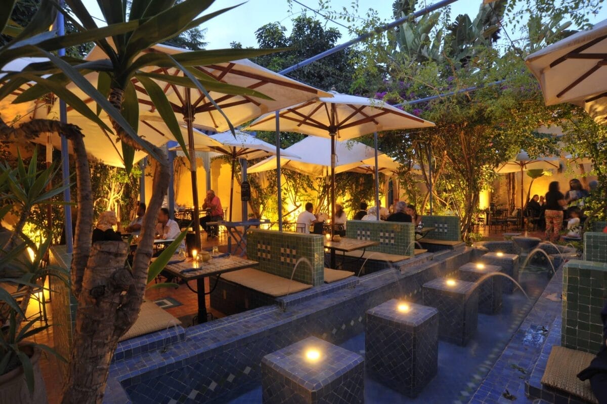 La Sqala est un charmant restaurant situé dans un jardin luxuriant, doté de tables élégantes et de parasols colorés.