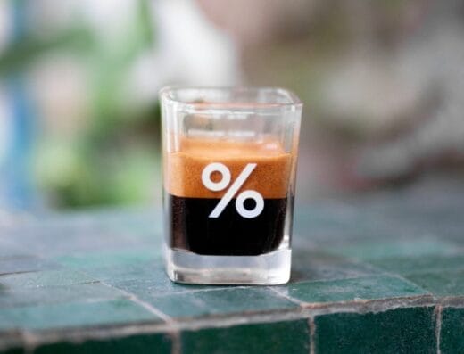 Un petit verre d'espresso avec le symbole « pour cent » imprimé dessus se trouve sur une surface carrelée de vert.