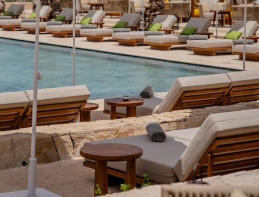 Une rangée de chaises longues au bord de la piscine avec des parasols blancs, des petites tables et des serviettes roulées surplombe la mer dans un restaurant du complexe.