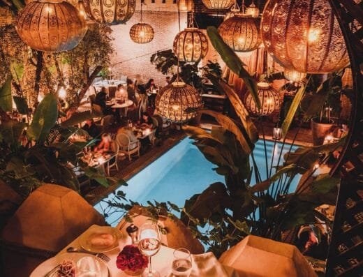 Un restaurant au décor du Moyen-Orient avec des lanternes suspendues complexes et un coin salon au bord de la piscine proposant un repas gastronomique et des boissons, éclairé par un éclairage d'ambiance doré - une oasis auto-conçue alliant hospitalité et luxe.