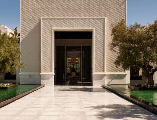 Un bâtiment moderne avec une grande entrée carrée est flanqué de verdure et de bassins réfléchissants, sur fond de ciel bleu clair. Les voitures Brouillon bordent les rues avoisinantes, ajoutant une touche d'élégance urbaine à la scène sereine.