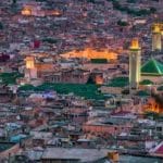 Vue aérienne d'un paysage urbain densément peuplé avec des mosquées et des toits illuminés au crépuscule, capturant le charme enchanteur de la vieille Fès, l'une des célèbres villes impériales du Maroc.