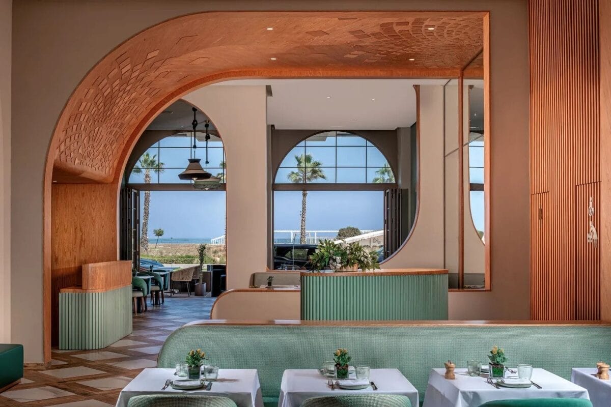 L'intérieur élégant du restaurant bénéficie d'un charme pomo dolce avec une décoration moderne, avec des arches en bois, des sièges verts et de grandes fenêtres encadrant une vue imprenable sur les palmiers et la mer.