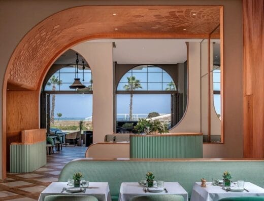 L'intérieur élégant du restaurant bénéficie d'un charme pomo dolce avec une décoration moderne, avec des arches en bois, des sièges verts et de grandes fenêtres encadrant une vue imprenable sur les palmiers et la mer.