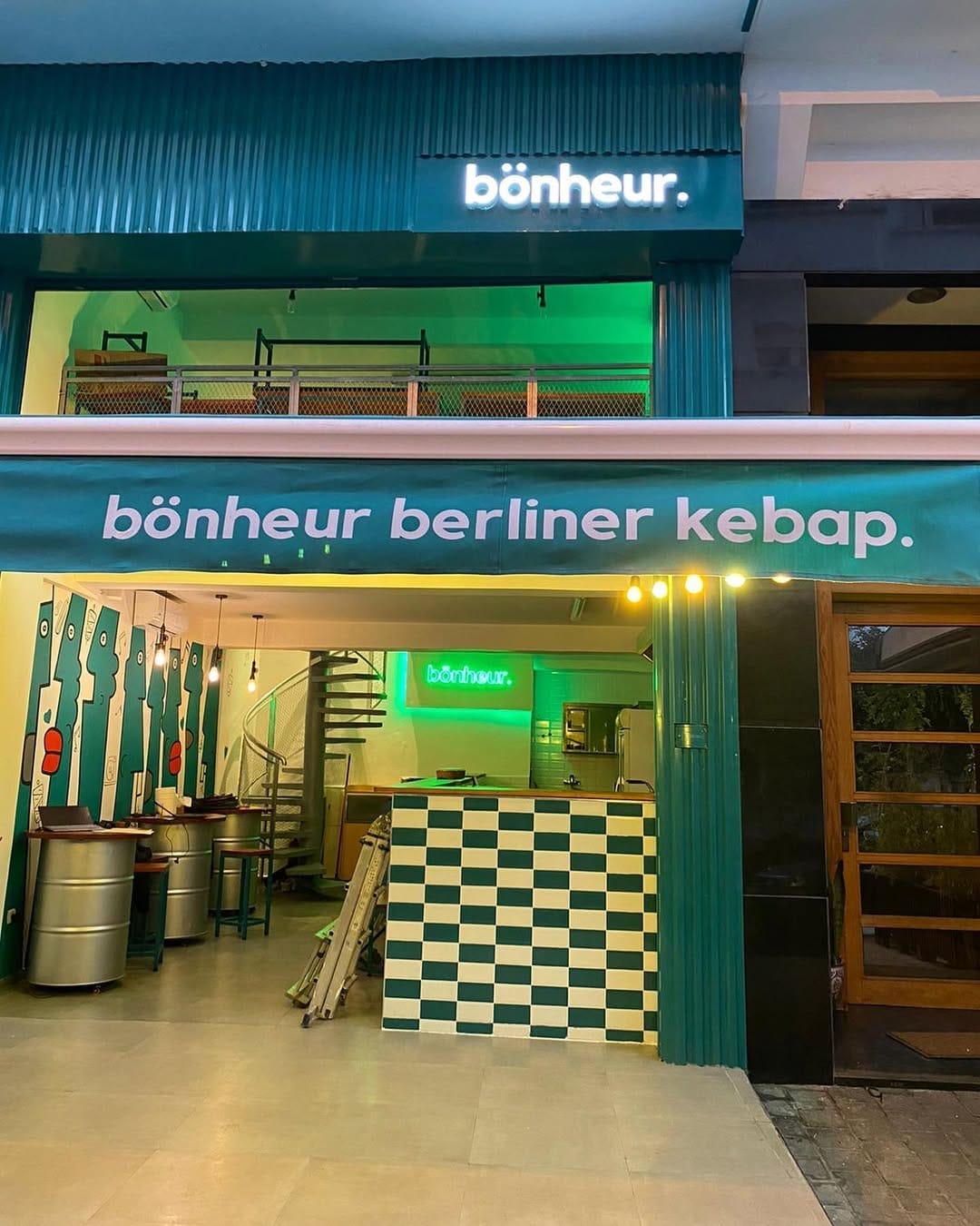 L'extérieur du « bonheur kebap » arbore un auvent et une signalétique verts. À l'intérieur, vous découvrirez un escalier en colimaçon, des murs verts et un comptoir à carreaux.