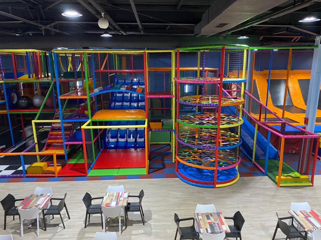 Aire de jeux intérieure avec structures d'escalade hautes et colorées et toboggans, idéale pour les enfants. Tables et chaises sont installées au premier plan, idéales pour des activités familiales à Marrakech.