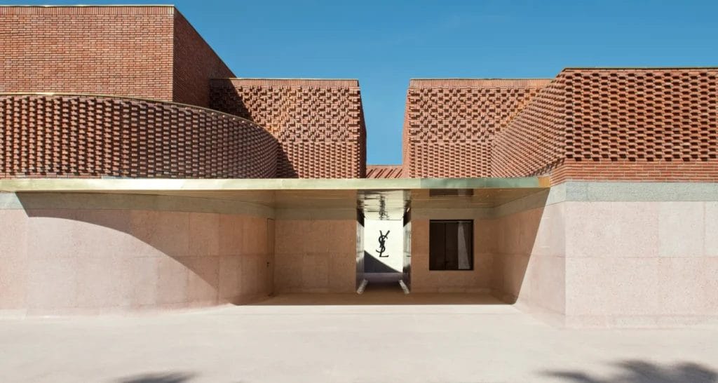 Un bâtiment moderne aux briques géométriques et à l'auvent doré sous un ciel bleu azur à Marrakech. Le logo d'une grande marque de mode apparaît sur un mur, offrant un cadre élégant aux familles profitant d'activités familiales dans cette ville animée.