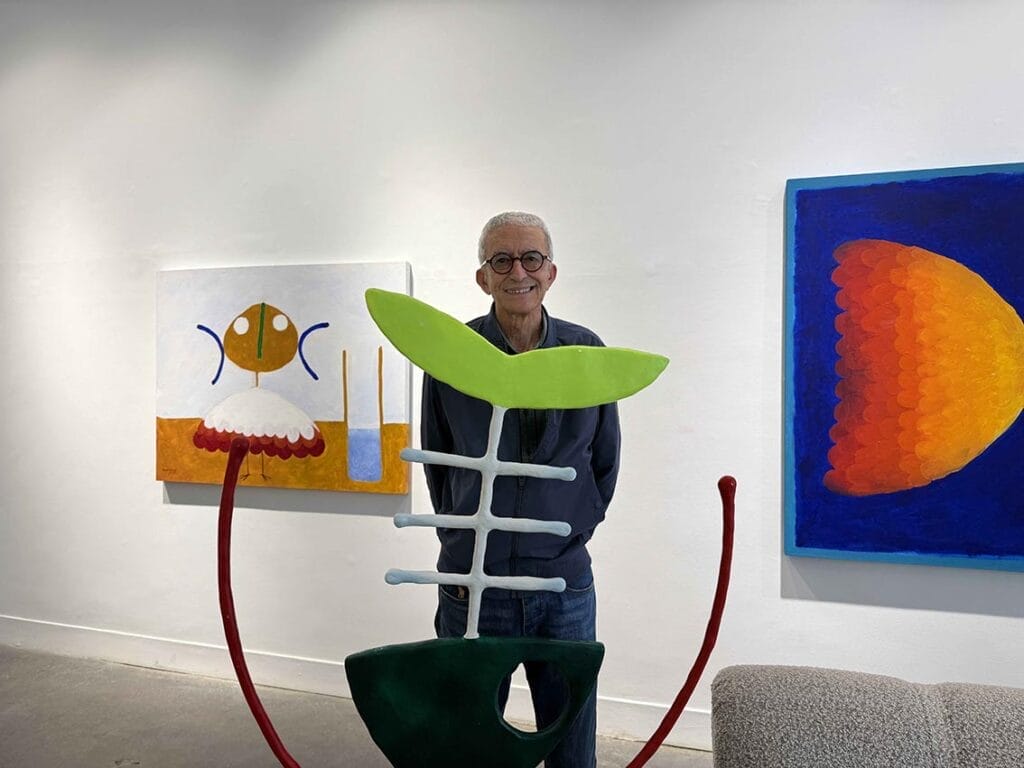 Un homme d'un certain âge se tient dans une galerie d'art, souriant, avec des sculptures et des peintures abstraites colorées exposées sur les murs derrière lui - un instantané parfait des sorties culturelles que Casablanca a à offrir.