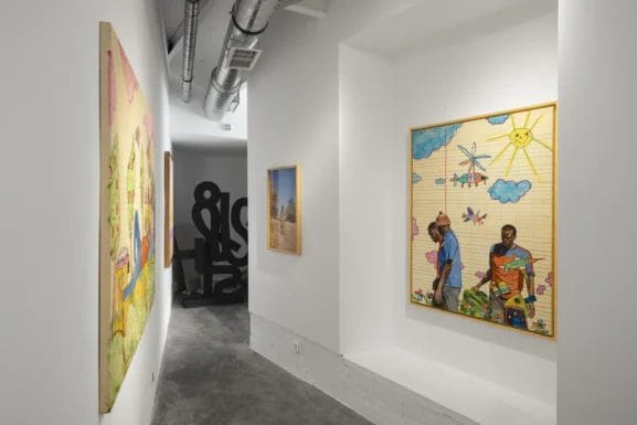 Un couloir de galerie d'art moderne - parfait pour les sorties culturelles à Casablanca - avec des peintures colorées encadrées sur des murs blancs, des sols en béton et des conduits apparents au plafond.